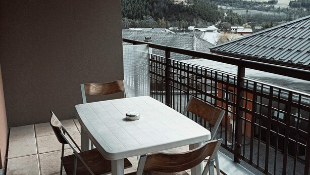 Een balkon met een tafel en stoelen, met uitzicht op een bergachtig landschap.
