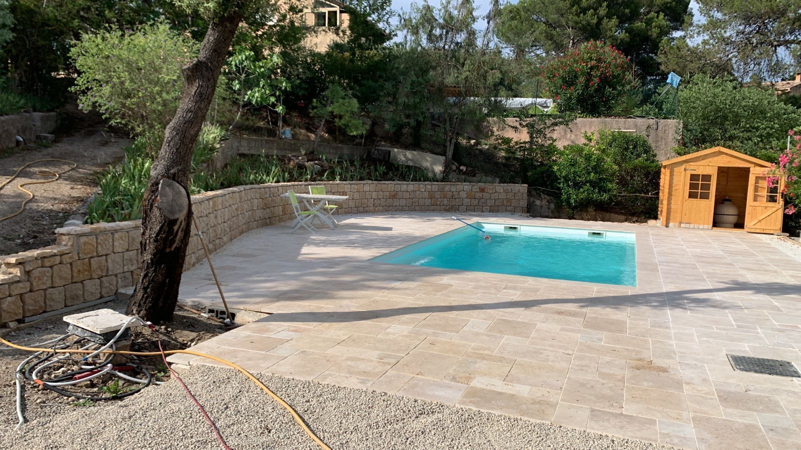 Una piscina con bordo in pietra, circondata da un muro in pietra e alberi.