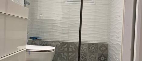 A bathroom with a toilet, shower, and a window.