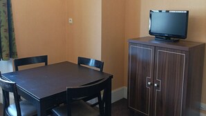A hotel room with a dark wooden table and chairs, a television on a cabinet, and a window with curtains. - T3 apartment in castle with pool and WIFI, pets allowed, 6 people (Jausiers)