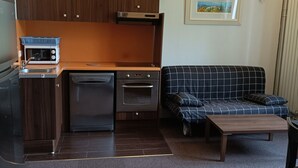 A compact living space with a kitchenette, a sofa, and a small table. - T3 apartment in castle with pool and WIFI, pets allowed, 6 people (Jausiers)