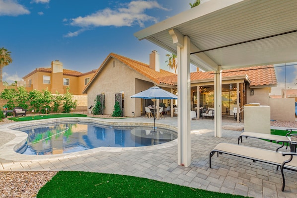 Une piscine à bord incurvé, entourée d’une terrasse dallée aménagée avec du mobilier d’extérieur et un espace salon abrité.