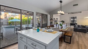 A modern kitchen with a large island, dining area with a wooden table, and a living room with a sofa. - Updated 3BR Scottsdale Home | Heated Pool, Putting Green, Fire Pit (Scottsdale)