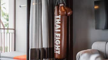 A punching bag labeled "THAI FIGHT" in a modern room with a grey sofa and a large window with curtains.