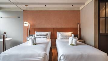 A hotel room with two beds, a wooden floor, a large mirror, and a window with blinds.