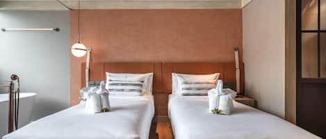 A hotel room with two beds, a wooden floor, a large mirror, and a window with blinds.