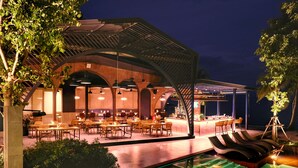 An outdoor dining area with tables and chairs, a pool with lounge chairs, and a bar area with a counter and seating. - Thai Fight Hotel (Koh Samui)