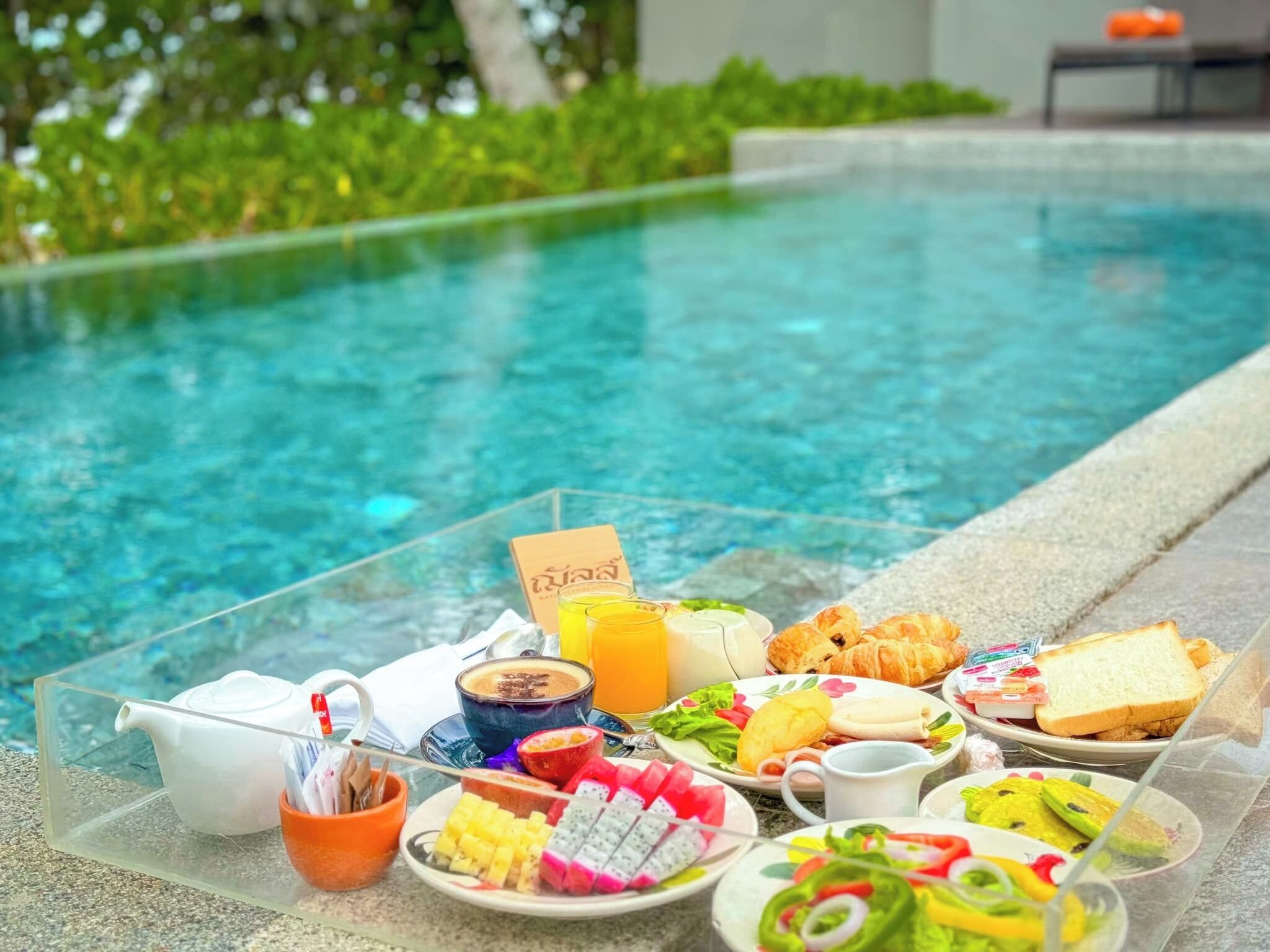 Un bufé de desayuno con diversas opciones de comida y una tetera junto a una piscina.