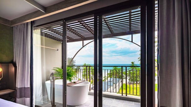 Habitación de hotel moderna con un amplio ventanal corredera que da a un balcón con vistas al océano y un jacuzzi.