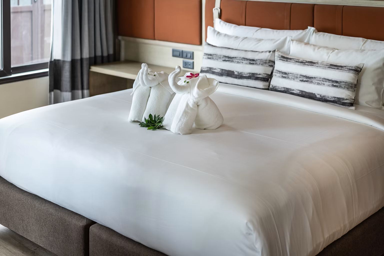 A neatly made bed with white linens, a headboard with pillows, and a small plant on the bed.