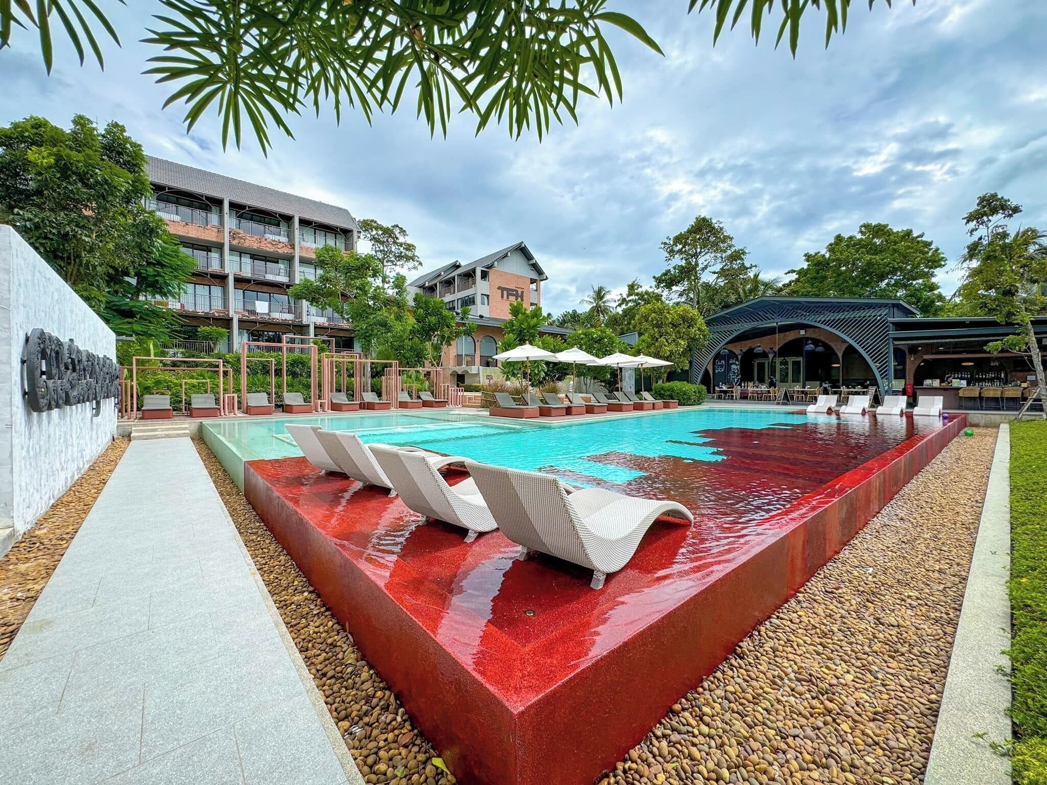 A swimming pool with lounge chairs, a bar area, and a building with balconies.