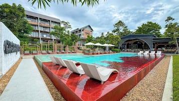 A swimming pool with lounge chairs, a bar area, and a building with balconies.