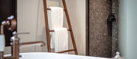 Un baño con una escalera de madera apoyada en una pared, una bañera blanca y un recipiente de vidrio sobre el mueble.
