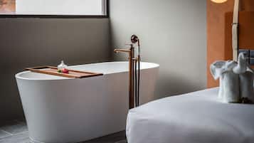 A modern bathroom with a freestanding bathtub, a wooden tray, and a small decorative item on the edge.
