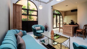 Una habitación amplia con un gran ventanal arqueado, un sofá teal confortable, un escritorio de madera y una mesa de centro de cristal.