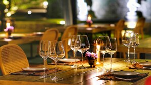 Una mesa de comedor preparada con varias copas de vino, platos y cubiertos, con una vela y flores sobre la mesa.