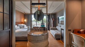 Una habitación de hotel moderna con un lavamanos grande y redondo, una cama con ropa blanca, un sofá y un comedor.