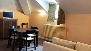 A dining area with a table and chairs, a sofa, a radiator, and a TV on a cabinet. - Cozy apartment, pets welcome - 6 guests (Jausiers)