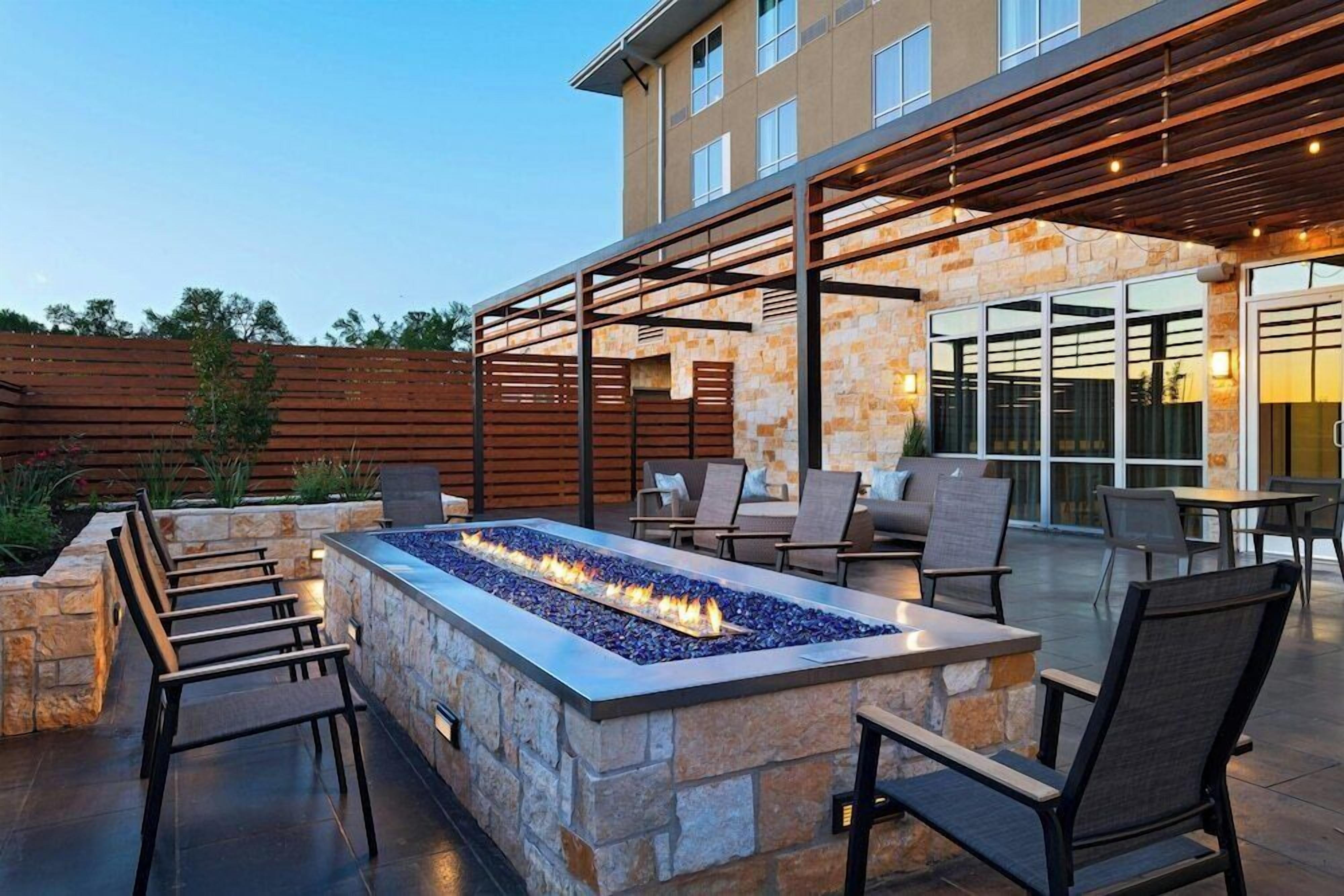 An outdoor patio with a stone fire feature, seating, and a covered area with tables and chairs.