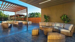 An outdoor patio with wicker furniture, a covered seating area, and a stone floor. - Courtyard Austin Dripping Springs (Dripping Springs)