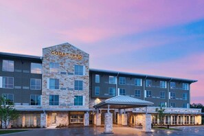 Um hotel Courtyard by Marriott com fachada de pedra, vários andares e entrada coberta.