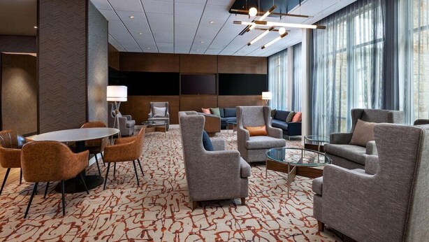 A modern hotel lobby with a round table, grey armchairs, and a patterned carpet. - Courtyard Austin Dripping Springs (Dripping Springs)