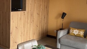 Et værelse med en væg af træpaneler, en grå sofa med et dekorativt pude, en sort gulvlampe og et fjernsyn monteret på væggen.