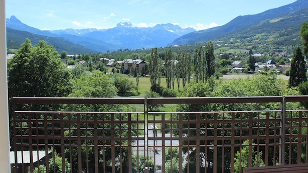 En balkon med udsigt over et bjerglandskab, en landsby og en vej.
