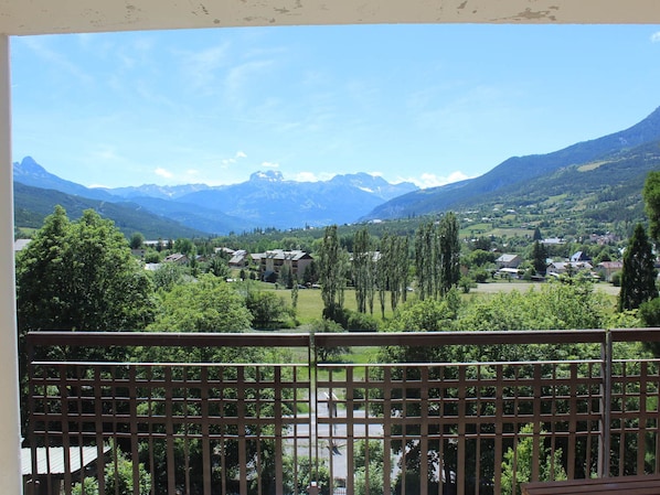 A balcony with a view of a mountainous landscape, a village, and a road.