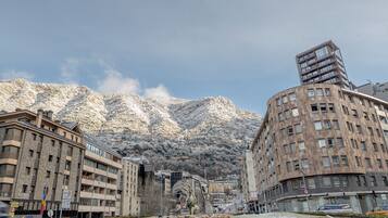 Un paisaje urbano con montañas nevadas al fondo, un edificio moderno de diseño único, y un edificio tradicional de varios pisos.