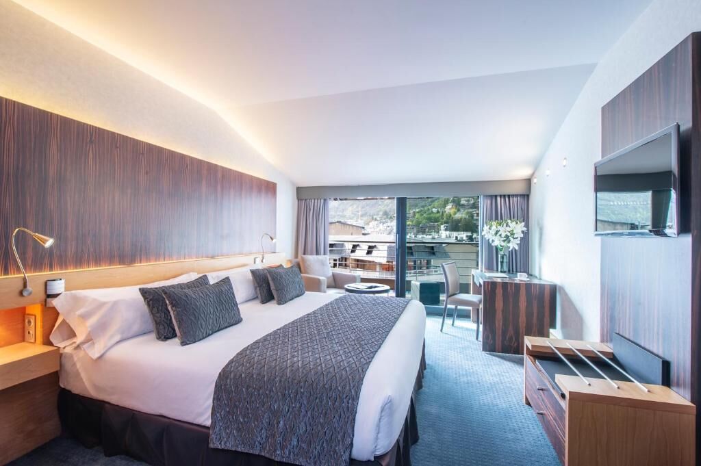 A modern hotel room with a large bed, a desk, a chair, and a TV.