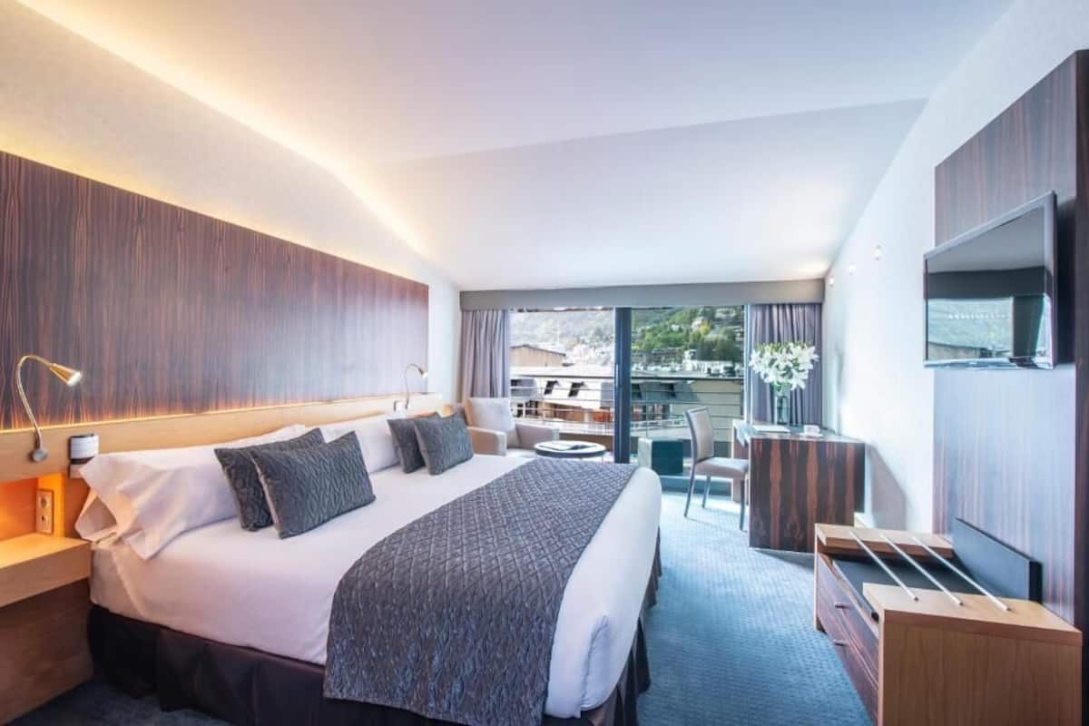 A modern hotel room with a large bed, a desk, a chair, and a TV.