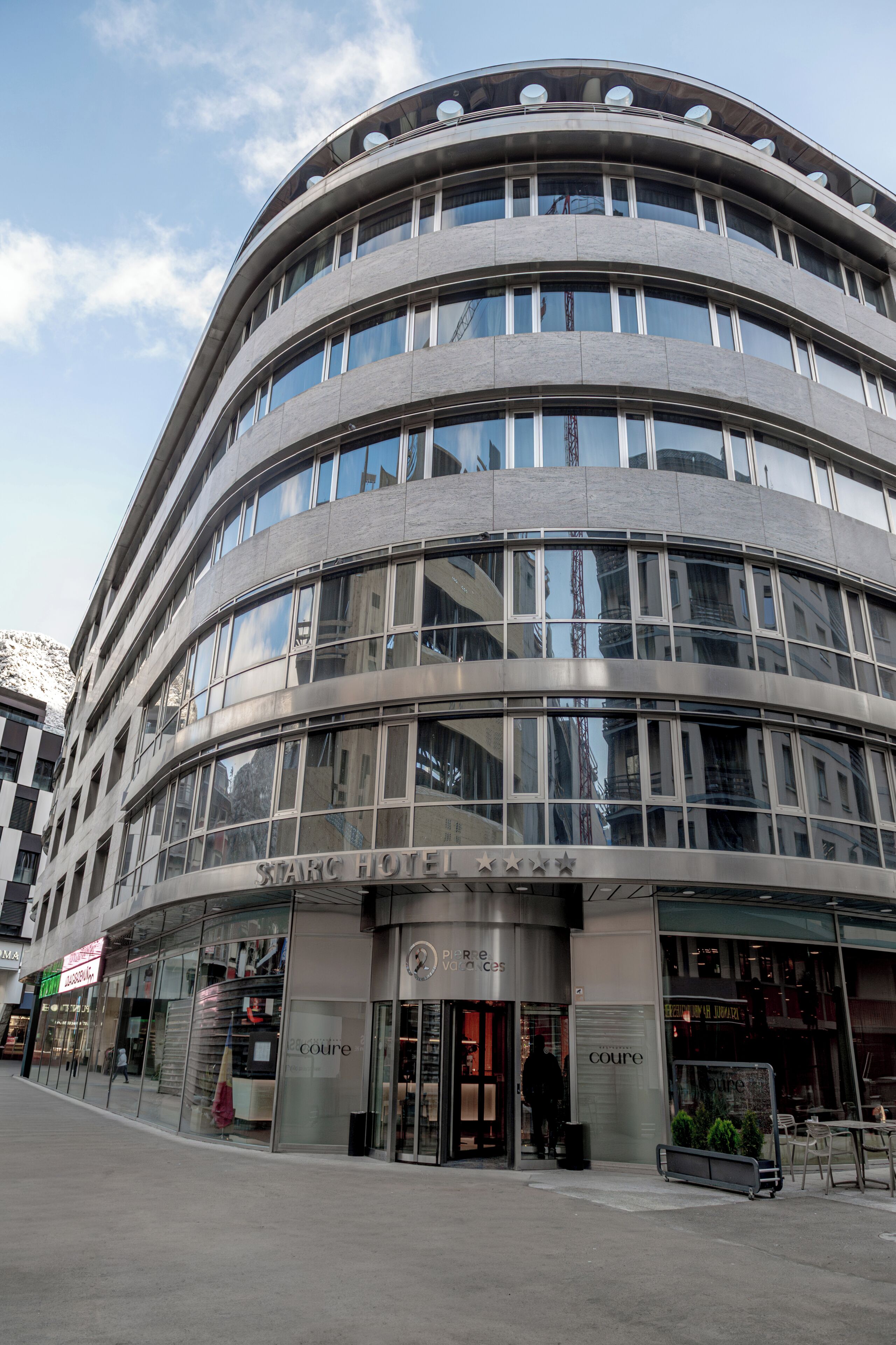A modern hotel with a curved facade, large windows, and a visible entrance.