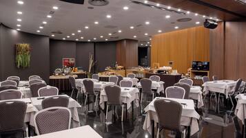 Un salón de conferencias con mesas, sillas, una zona de bufé y un escenario con proyector.