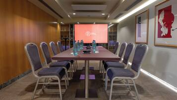 A conference room with a long table, chairs, and a screen displaying a logo.