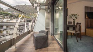 Un balcon avec vue sur les bâtiments et les montagnes, une table avec une chaise et un vase rempli de fleurs.