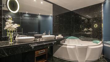 A modern bathroom with a large oval bathtub, a double sink vanity, and a large mirror with integrated lighting.