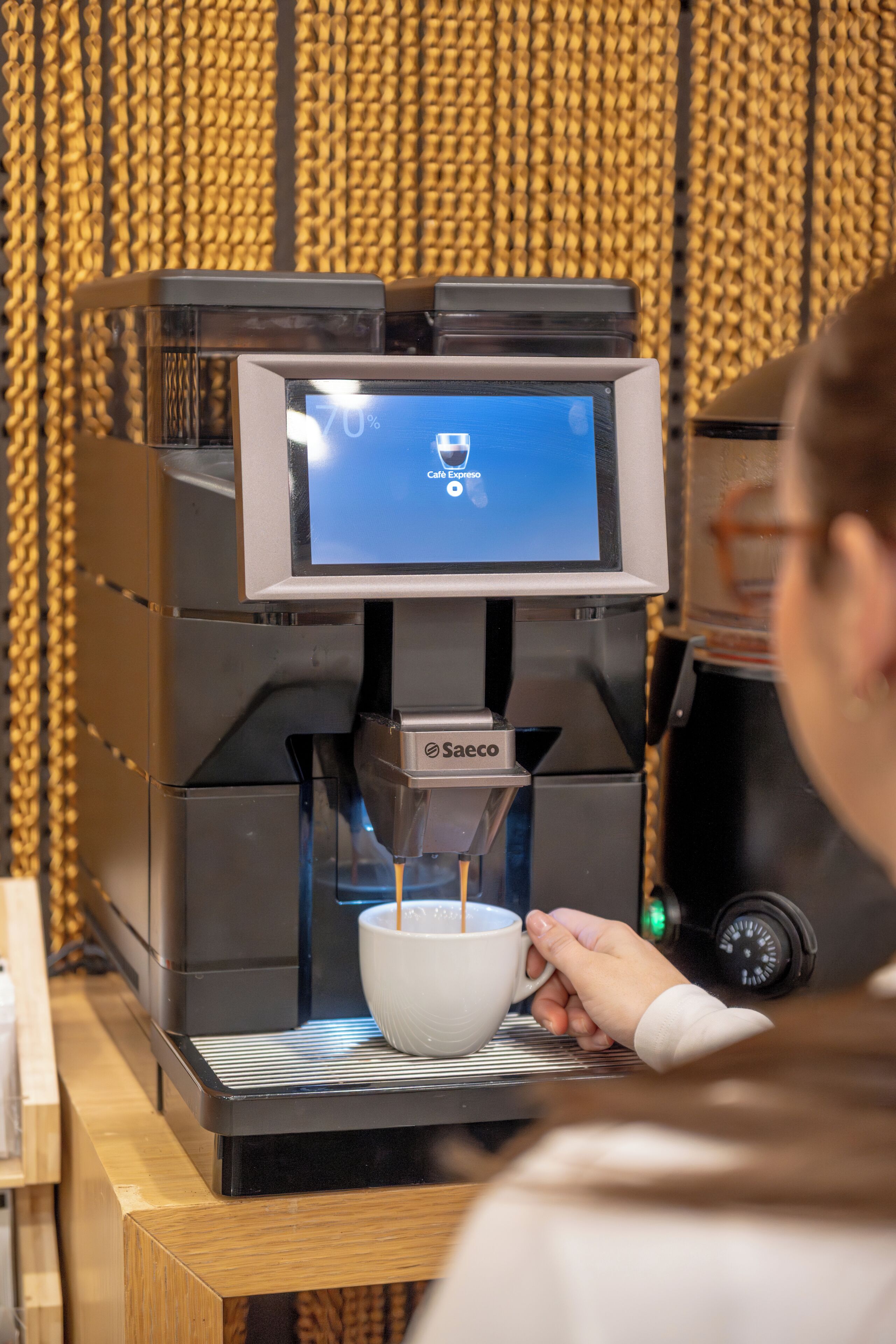 Una macchina per il caffè con un display digitale, una tazza e una persona che la tiene.