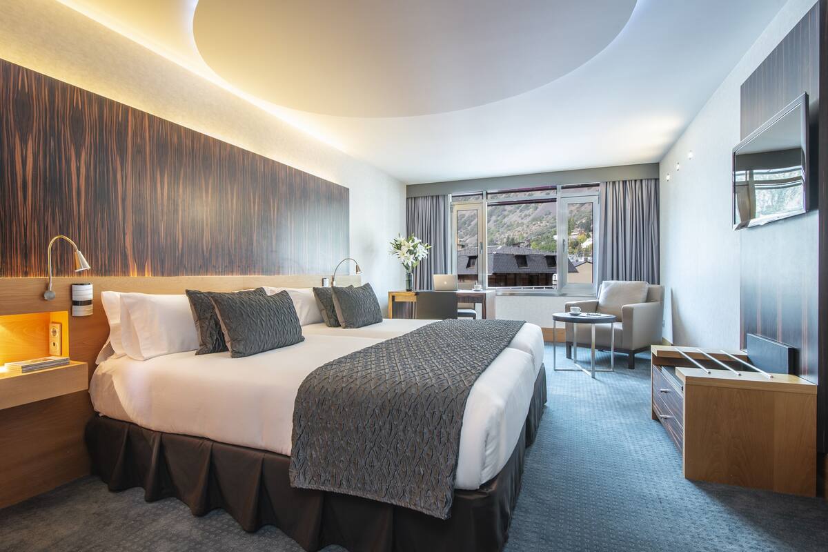 Une chambre d’hôtel moderne avec un grand lit, des tables de chevet, un bureau, une chaise et un téléviseur.