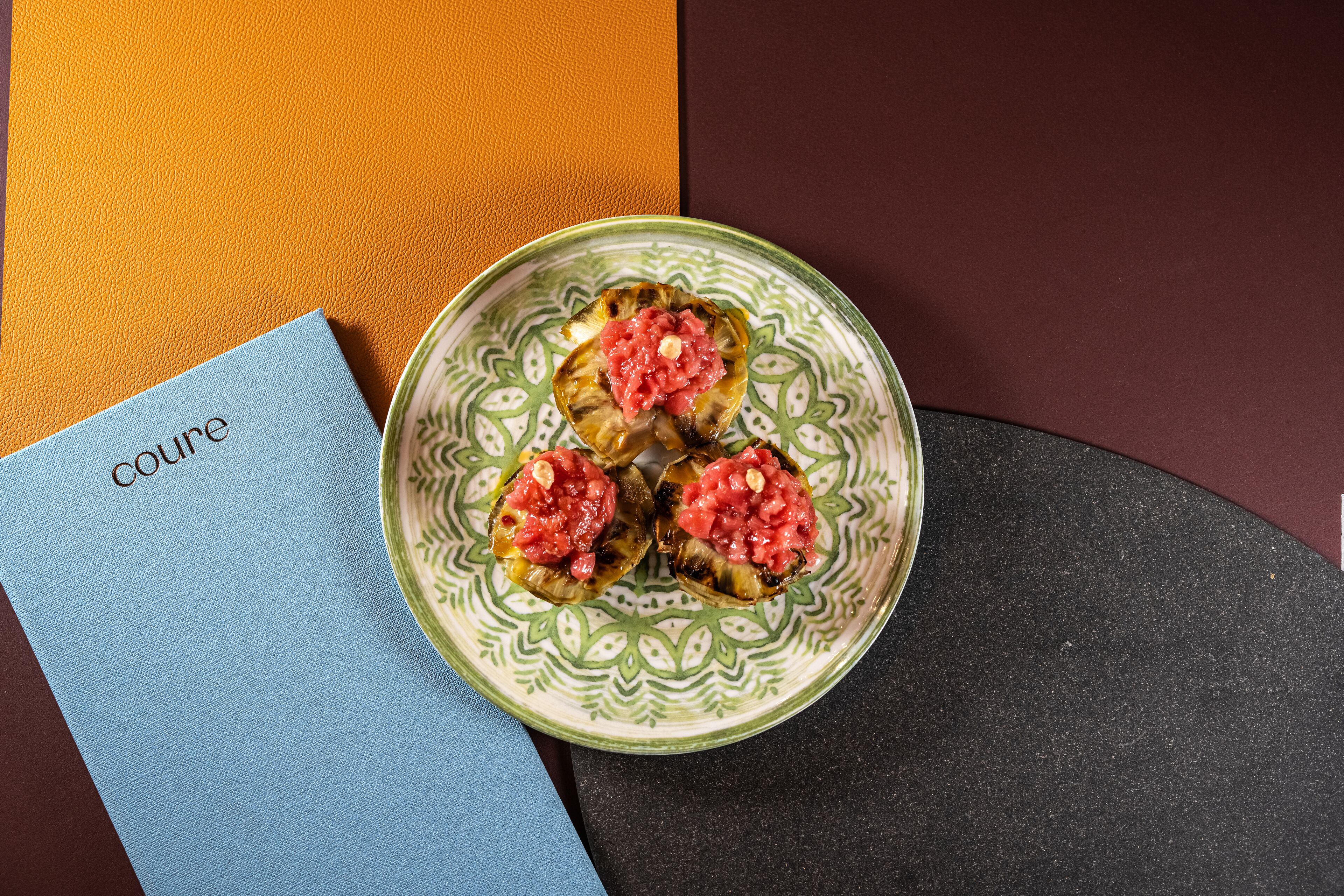 Une assiette décorative contenant trois champignons farcis, posée sur une table avec une serviette bleue et un livre intitulé « Cuisine » à côté.