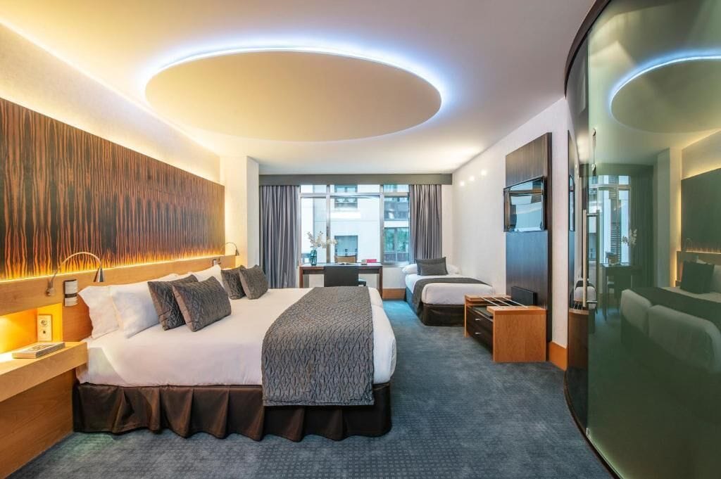 A modern hotel room with a large bed, a desk, a chair, and a view of the city.