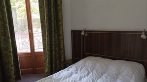 A bedroom with a wooden headboard, a white bedspread, and a view of a balcony through a window with green curtains. - 2-BR Apartment in Castle in Jausiers for 6, balcony, pets allowed (Jausiers)