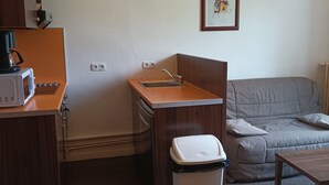 A compact room with a kitchenette, a sofa, a small table, and a trash bin. - 2-BR Apartment in Castle in Jausiers for 6, balcony, pets allowed (Jausiers)