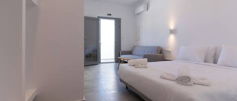 A modern hotel room with a large bed, a sofa, a small table, and a door leading to a balcony.