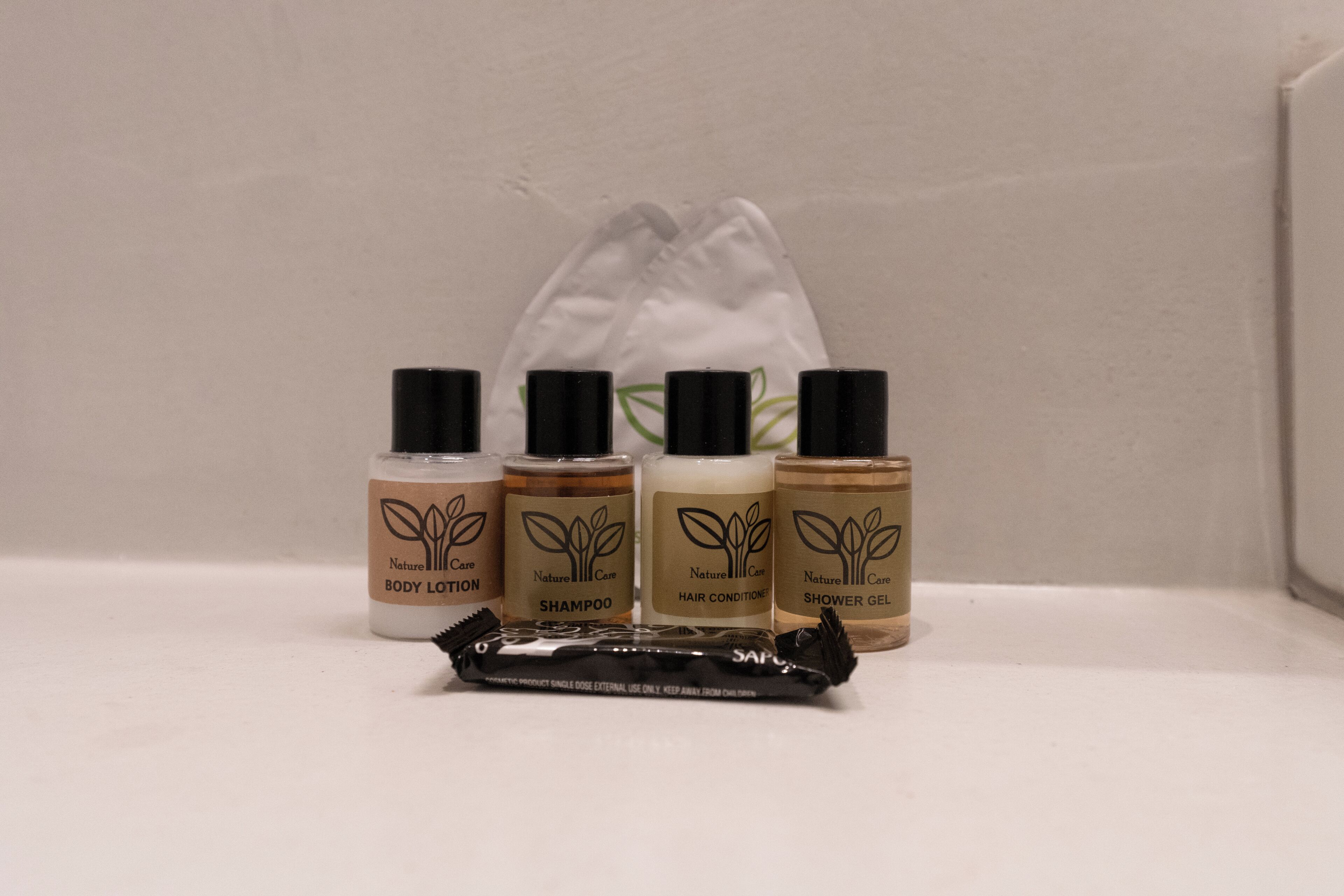 A set of Naturell Care body lotion, shampoo, hair conditioner, and shower gel bottles on a white surface.