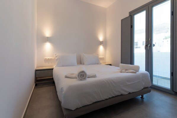 Un dormitorio moderno con una cama grande, dos lámparas de noche, un banco empotrado y un ventanal corredizo al exterior.