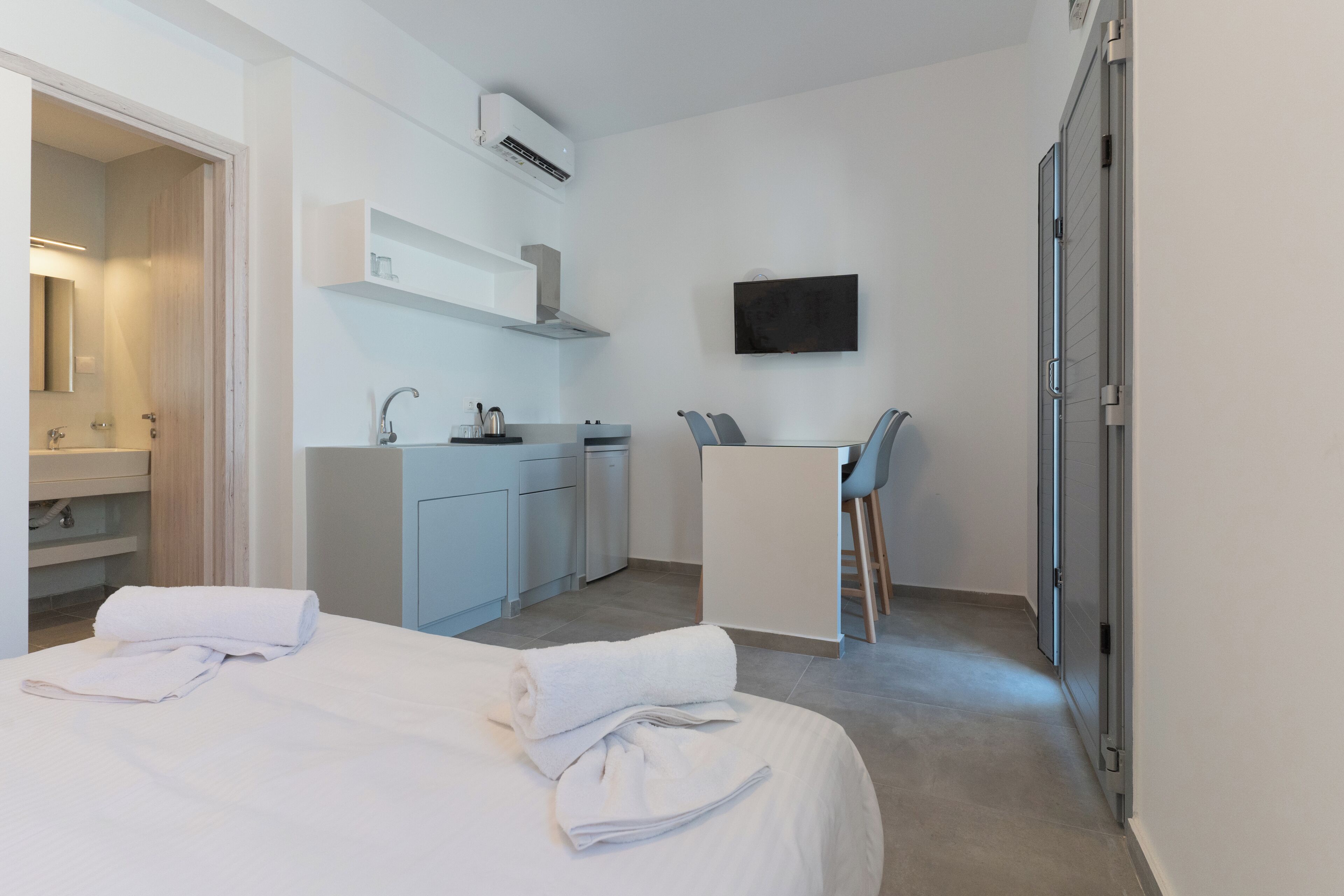 A hotel room with a bed, a kitchenette, a desk, and a TV.