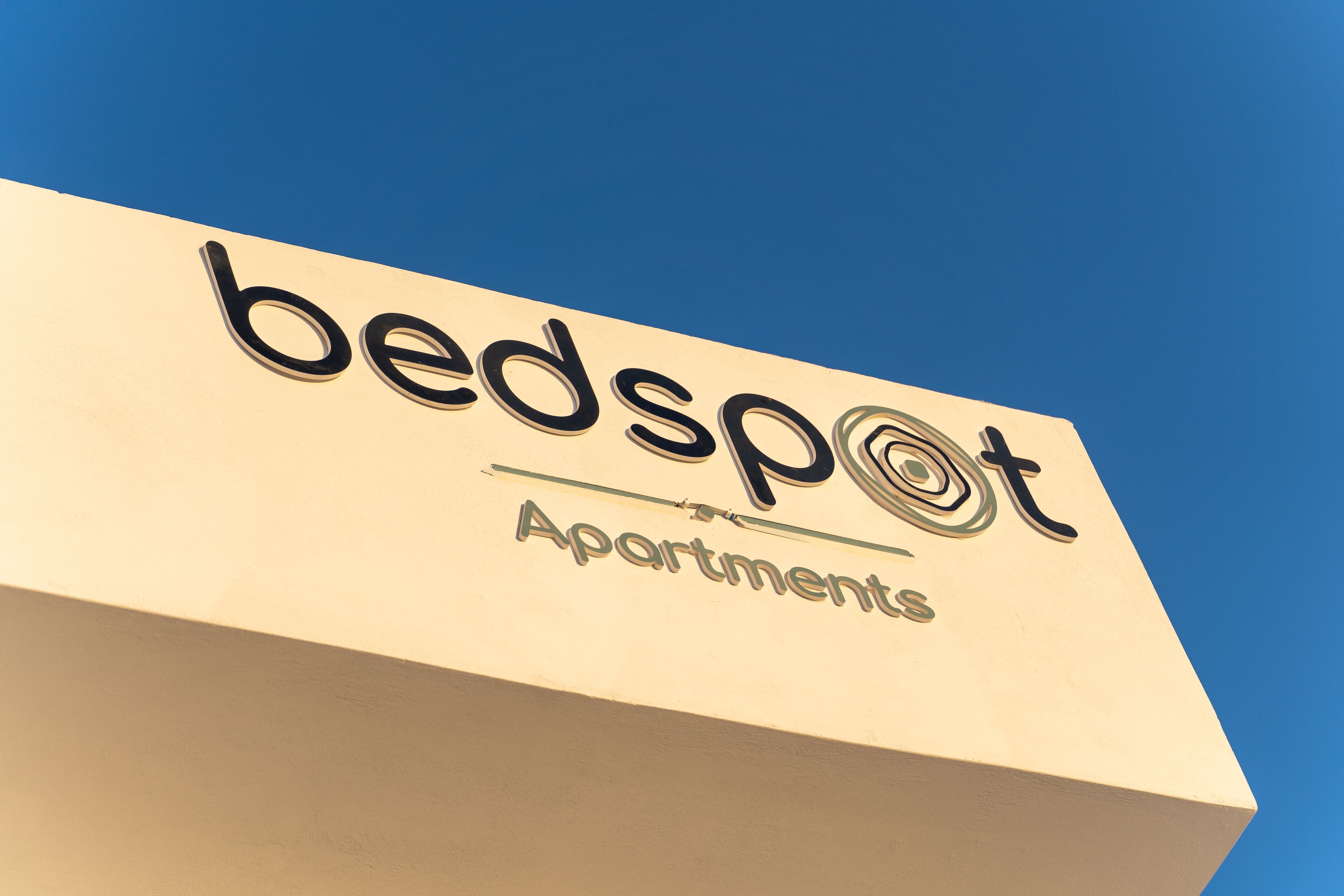 A sign for 'bedspot Apartments' with a clear blue sky in the background.