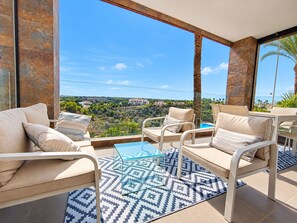 Ein Balkon mit einem Glastisch, beigen Sofas und einem gemusterten Teppich.