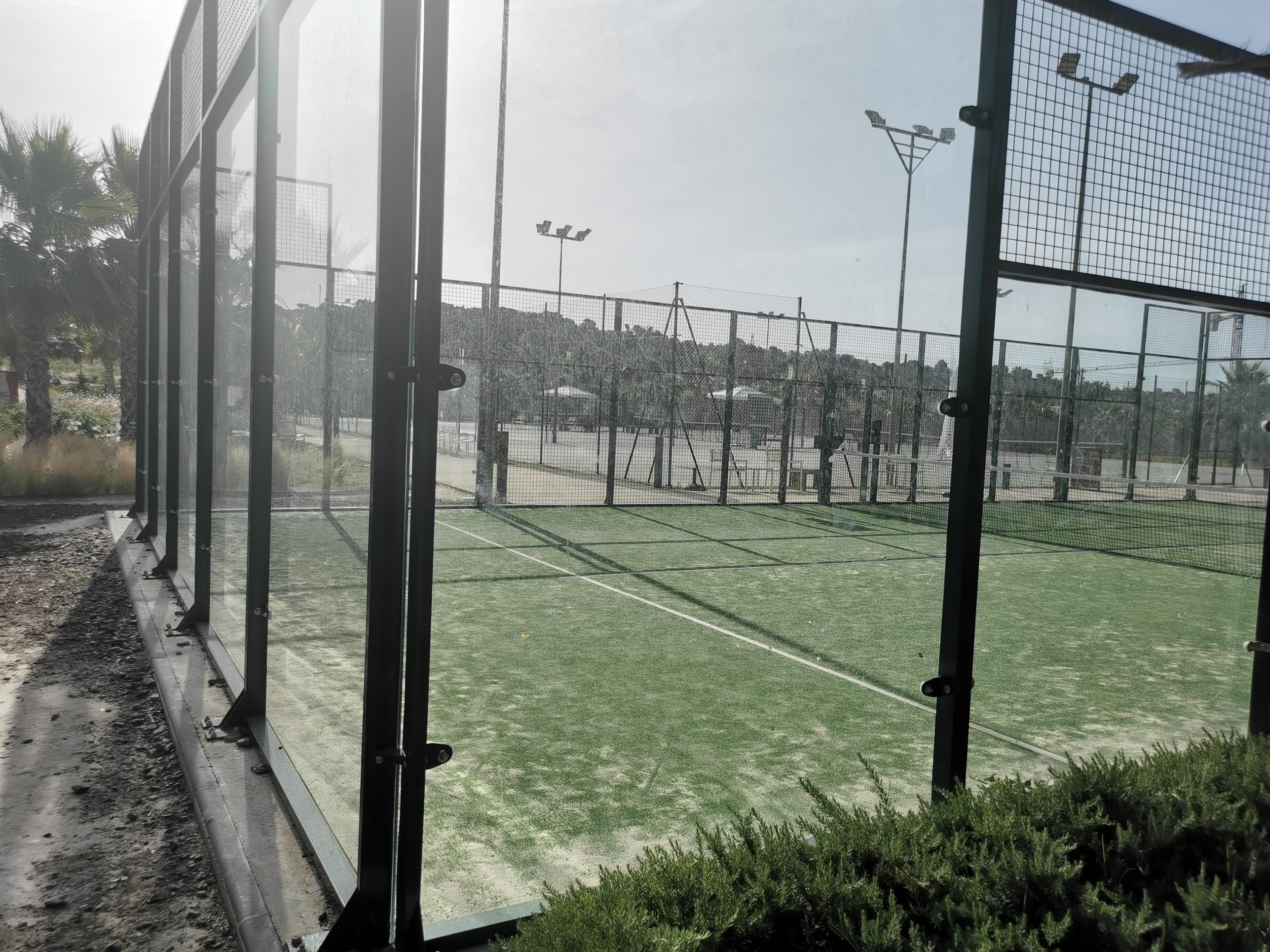 A tennis court with a net, surrounded by a fence, and a clear sky.